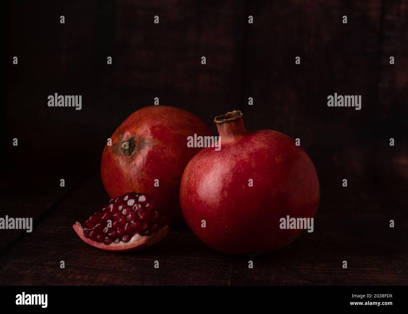 Saftig reife Granatäpfel von dunkelroter Farbe auf dunklem Grund mit einem kleinen Stück abgebrochenem Granatapfel mit Fruchtkörnern. Stockfoto