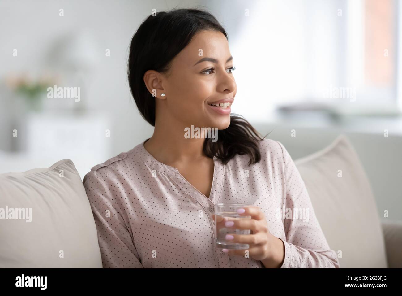 Glückliche hübsche junge Mischfrau trinkt ein Glas Wasser Stockfoto