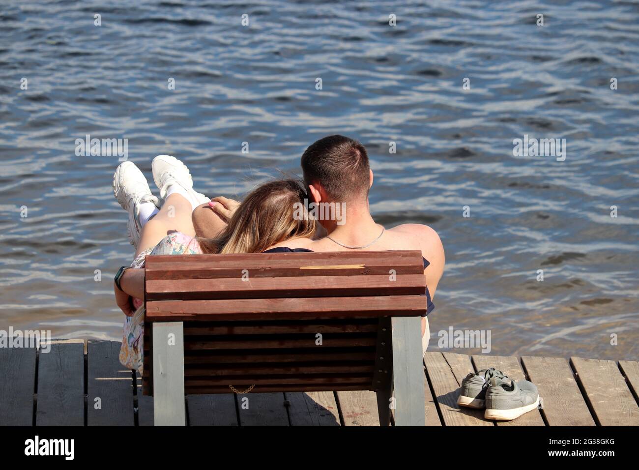 Ein junges Paar umarmt sich in einem hölzernen Liegestuhl am Strand. Romantischer Urlaub, Sommerurlaub an einer Meer- oder Flussküste Stockfoto