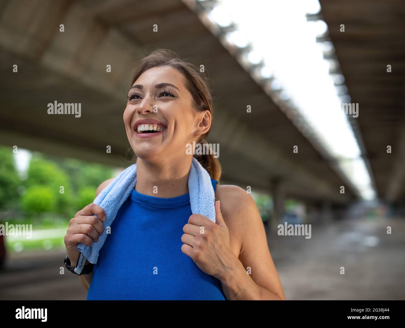 Fit Mädchen mit einem Handtuch, um Schweiß nach dem Training zu wischen. Lächelnder Sportler, der sich unter der Brücke ausruhen kann. Stockfoto