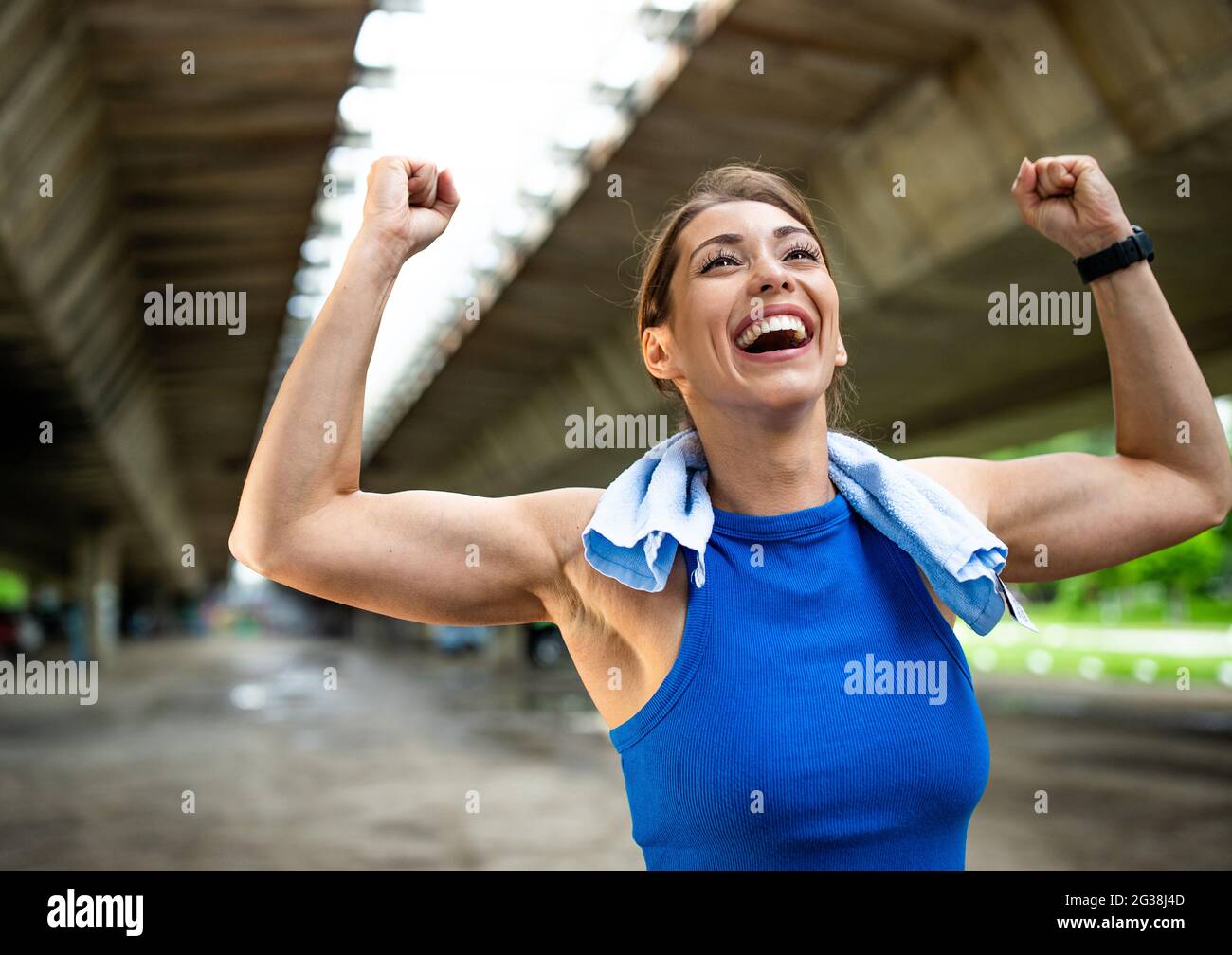 Junge Frau glücklich wegen Erfolg Sieg nach dem Training. Sportler, der nach dem Laufen mit einem Handtuch am Hals Schweiß abwischt. Stockfoto