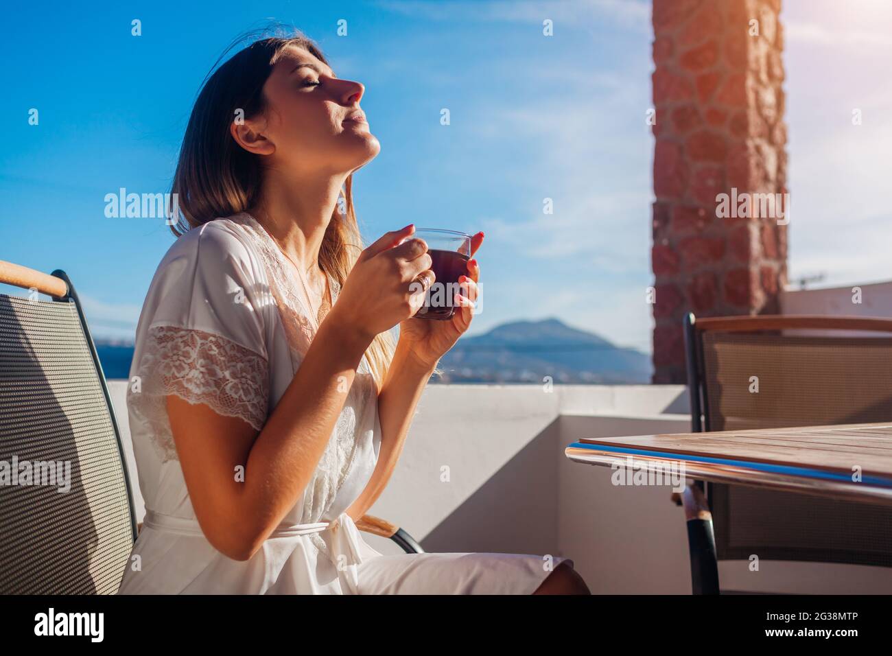 Frau, die sich auf der Hotelterrasse entspannt, trinkt morgens einen Kaffee und genießt die Berglandschaft von Santorini in Akrotiri. Sommerurlaub Stockfoto Frau, die sich auf der Hotelterrasse entspannt, trinkt morgens einen Kaffee und genießt die Berglandschaft von Santorini in Akrotiri. Sommerurlaub Stockfoto