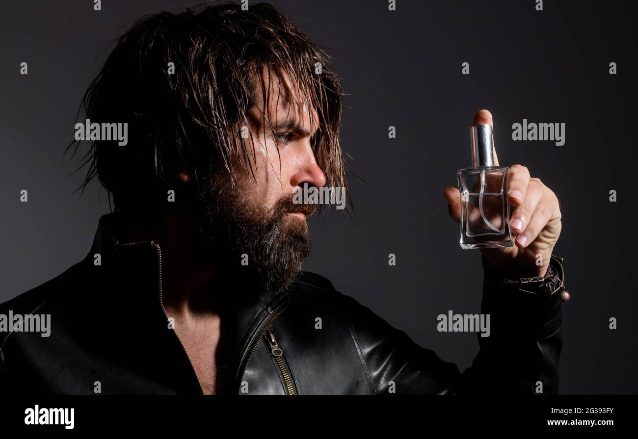 Bärtiger Mann in Lederjacke mit Flasche Parfüm oder köln. Kosmetikwerbung. Stockfoto