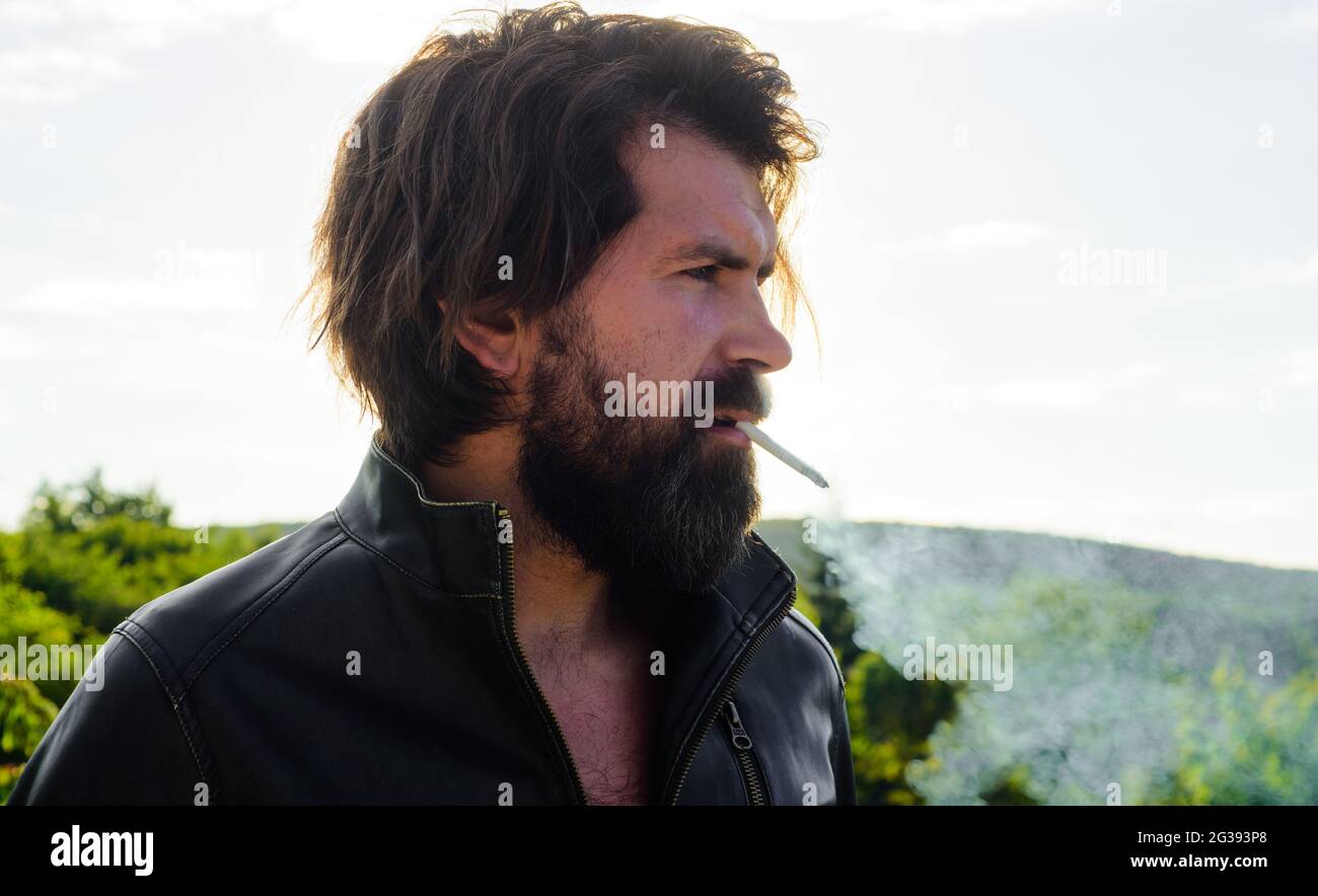 Bärtiger Mann, der raucht. Schöne stilvolle Male in Lederjacke mit Zigarette. Nikotinsucht und schlechte Gewohnheiten. Stockfoto