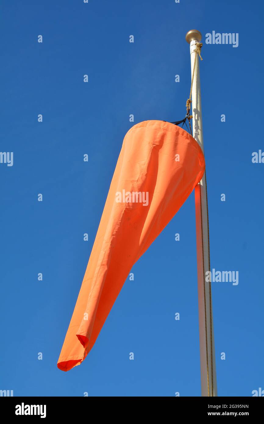 Leuchtend orangefarbene Windsocke, die im Wind gegen einen schlichten blauen Himmel weht Stockfoto