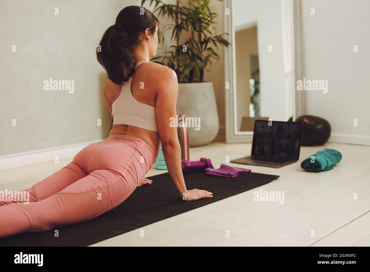 Eine Frau, die sich die Online-Trainingseinheit auf ihrem Laptop ansieht. Frau in Fitness-Kleidung macht Yoga beobachten Online-Kurs zu Hause. Stockfoto