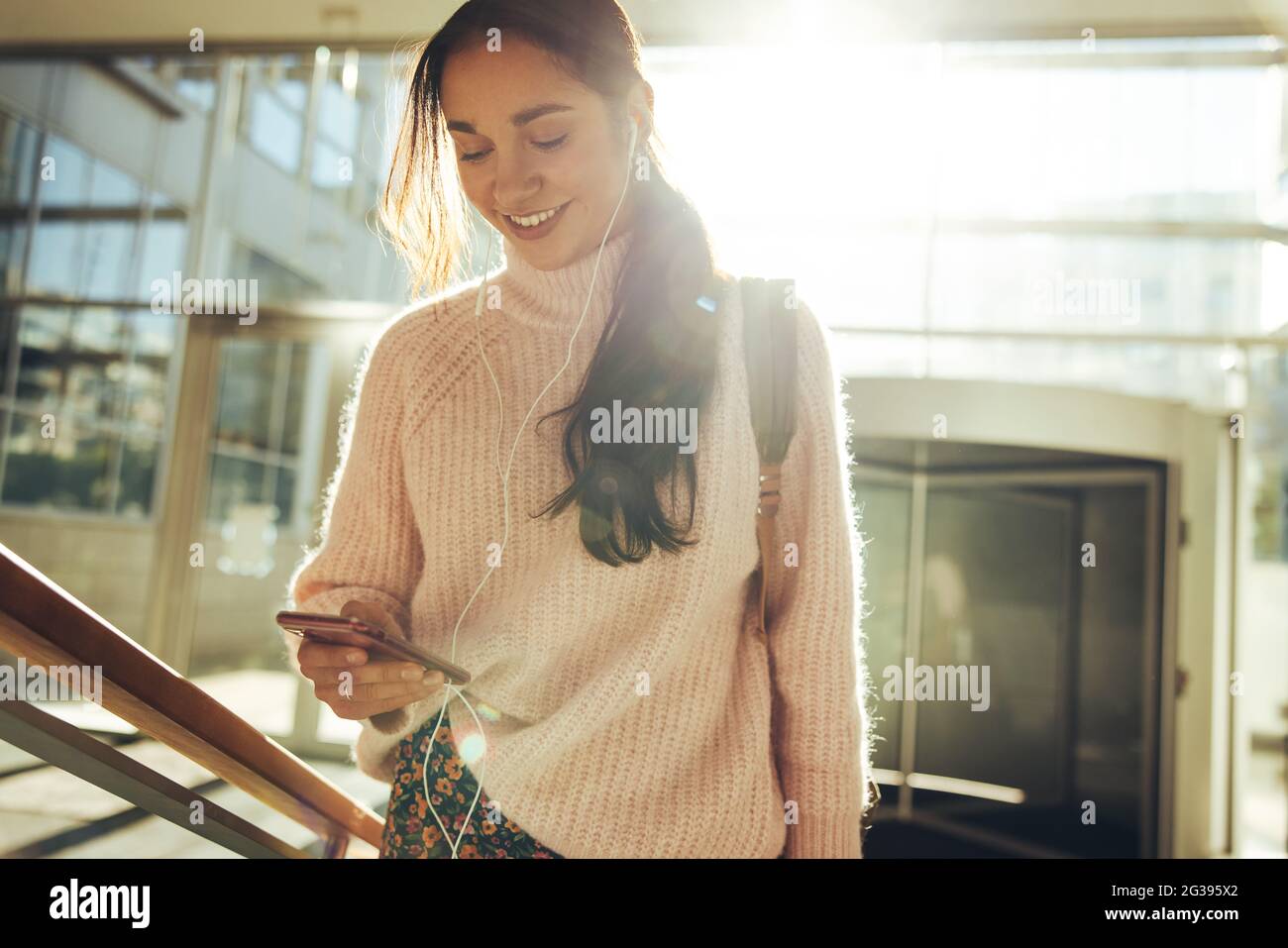 Junge Frau, die Social Media überprüft, bevor sie zum College geht. Student klettert Treppen und schaut auf das Mobiltelefon. Stockfoto