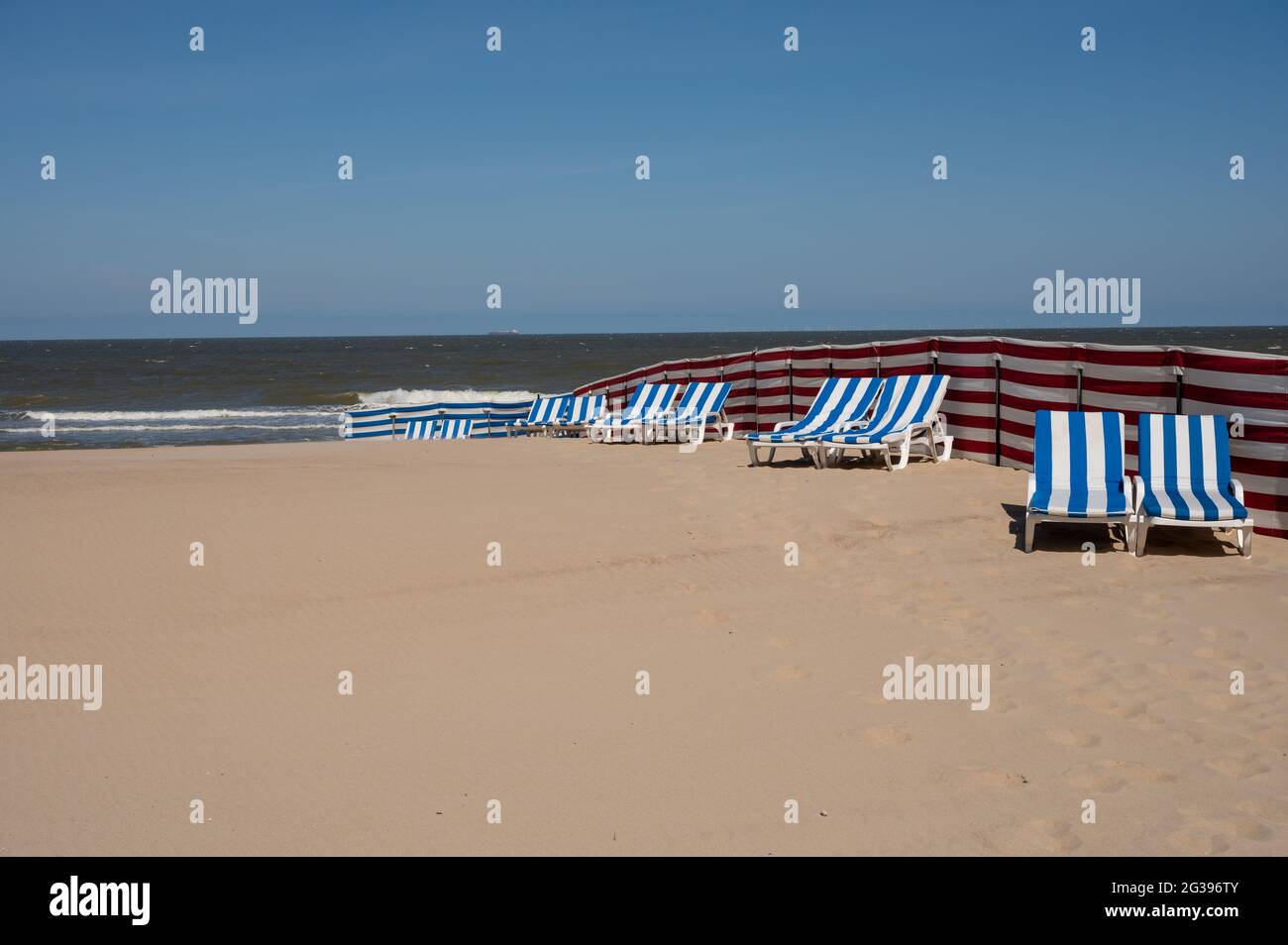 Leere blau-weiße Sonnenliegen am gelben Sandstrand in der kleinen belgischen Stadt De Haan oder Le Coq sur mer, Luxus-Urlaubsziel, Sommerferien Stockfoto