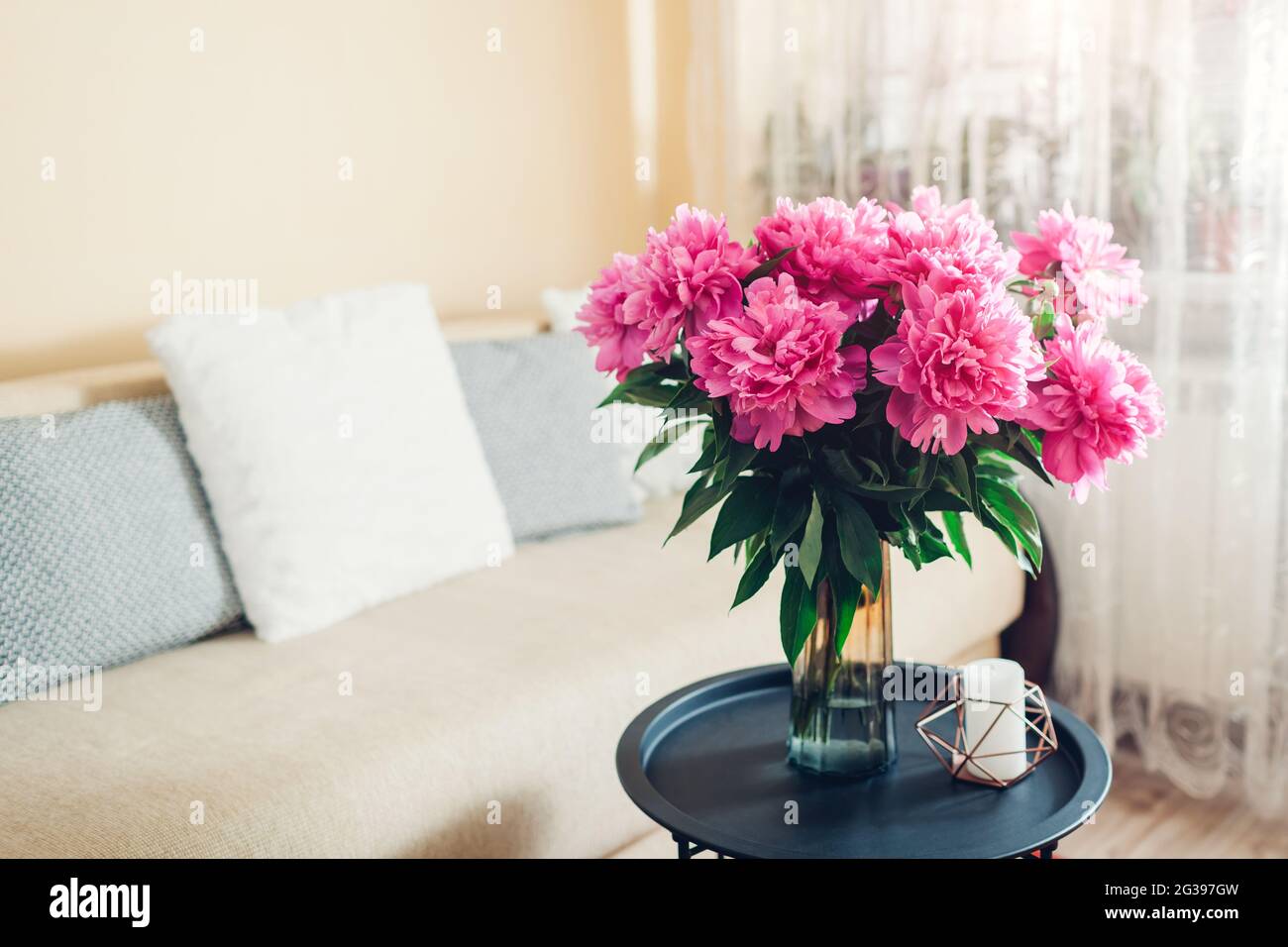 Inneneinrichtung und Inneneinrichtung. Frische rosa Pfingstrosen Blumen in Vase im Wohnzimmer von der Couch. Blumenstrauß auf dem Couchtisch Stockfoto