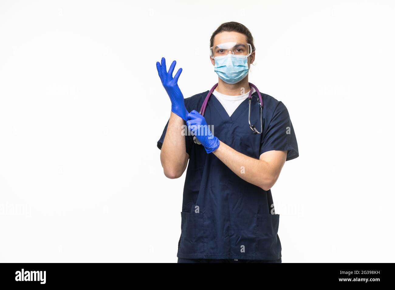 Der Arzt zieht Handschuhe an und trägt eine medizinische Maske auf weißem Hintergrund. Medizinisches Konzept Corona Virus Stockfoto