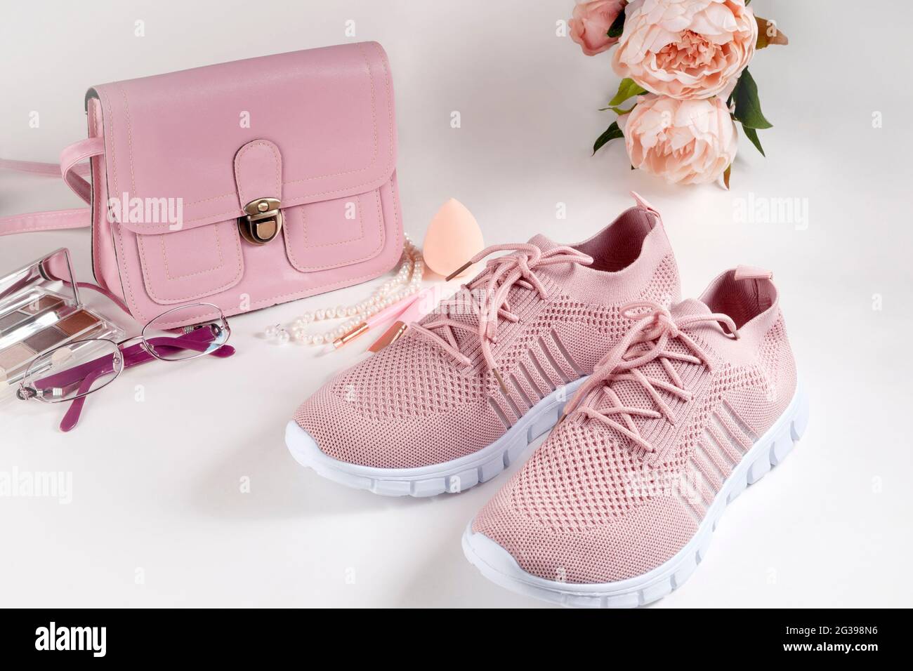 Layout auf weißem Hintergrund. Eine kleine Handtasche, eine Brille, eine Uhr und leichte Sommerschuhe in rosa und lila Farben. Stockfoto