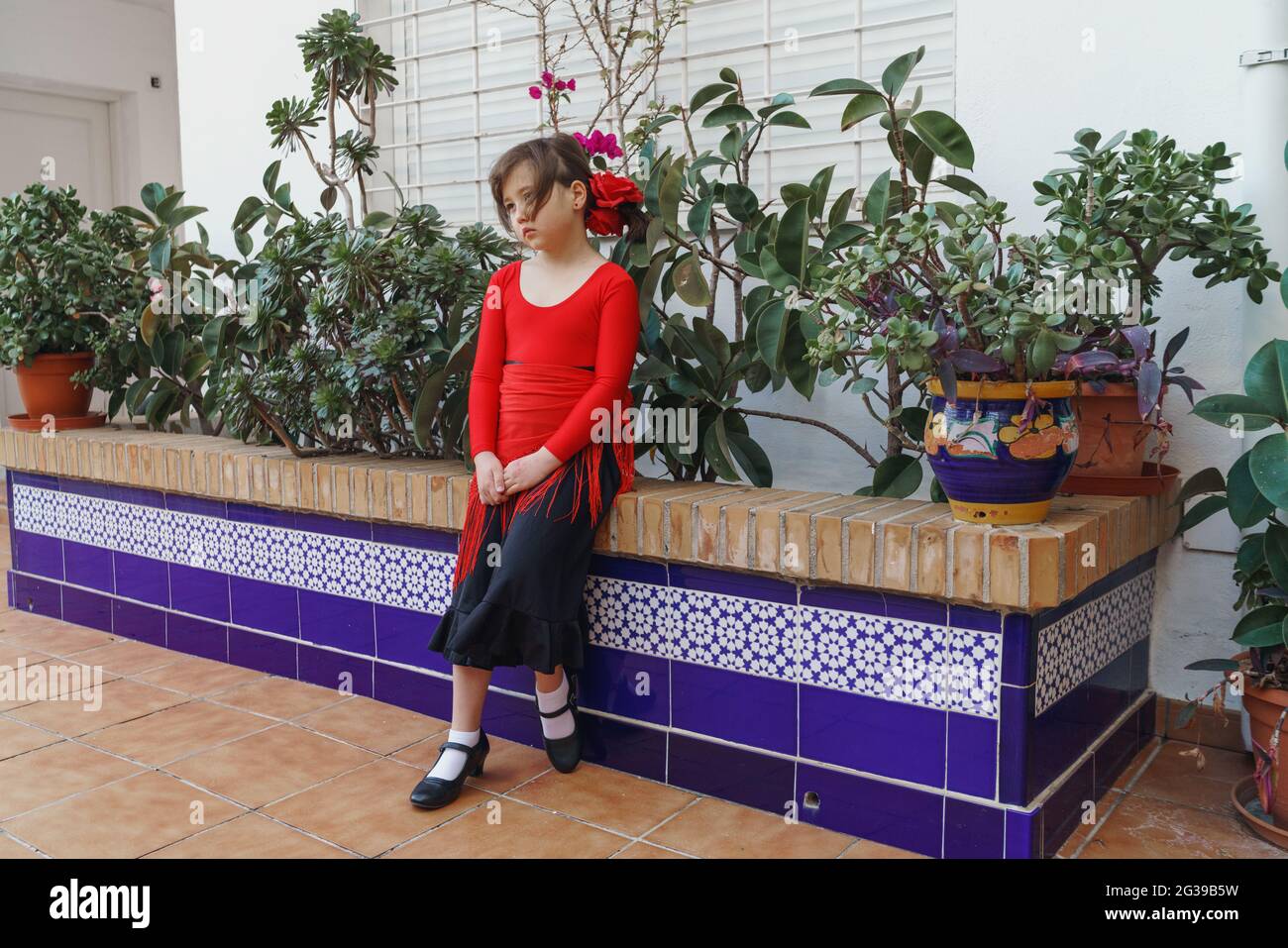 Kleines Mädchen, das zwischen heimischen Pflanzen sitzt Stockfoto