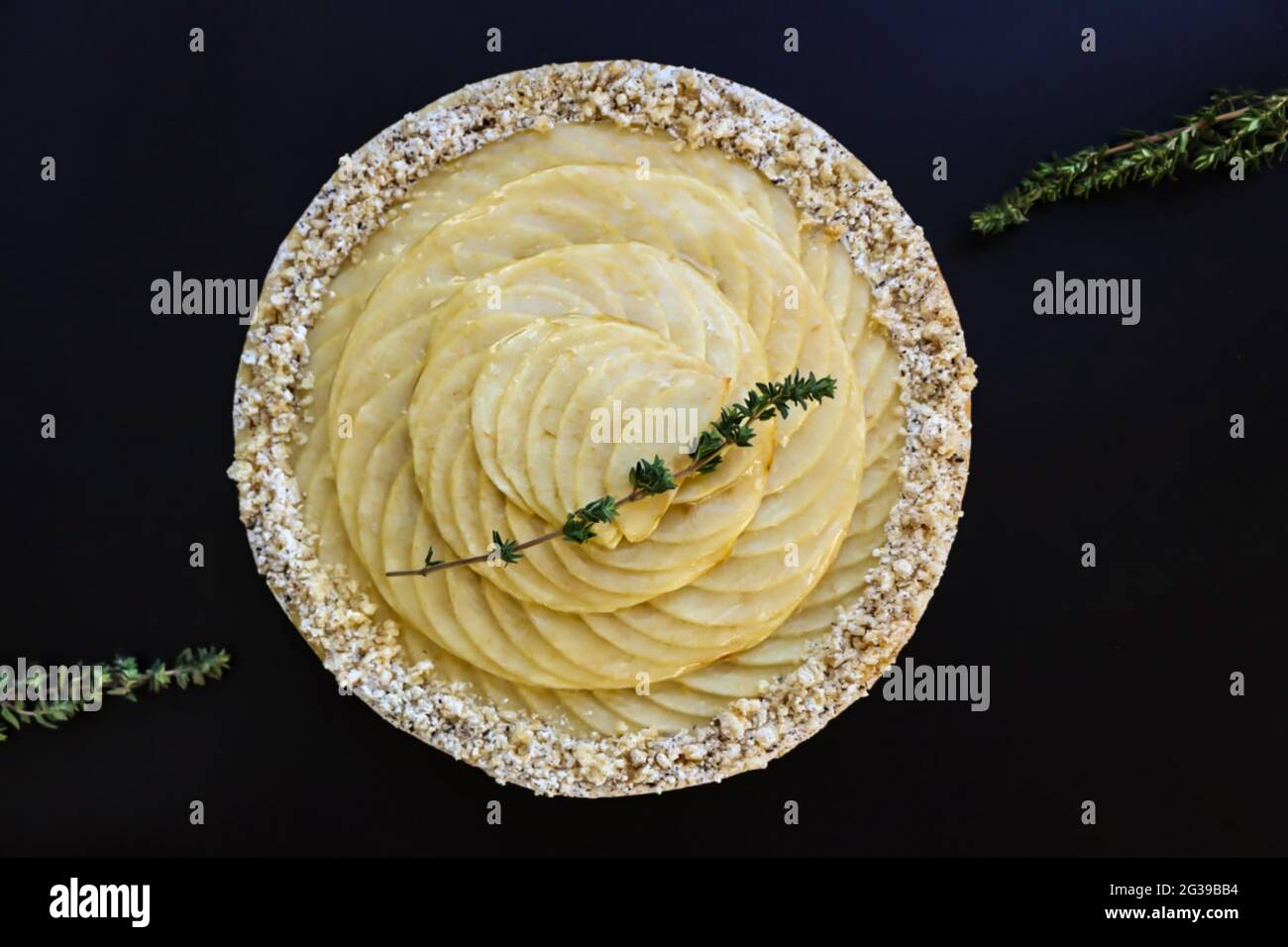 Runde Apfeltarte mit drei Thymianzweigen auf schwarzer Schrift Draufsicht Stockfoto