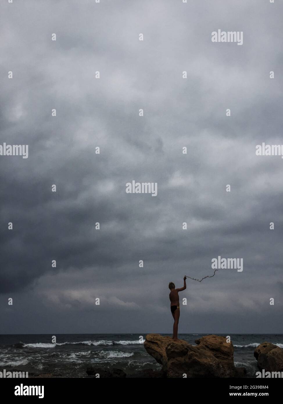 Ein Junge steht bei stürmischem Wetter auf Stein am Strand Stockfoto