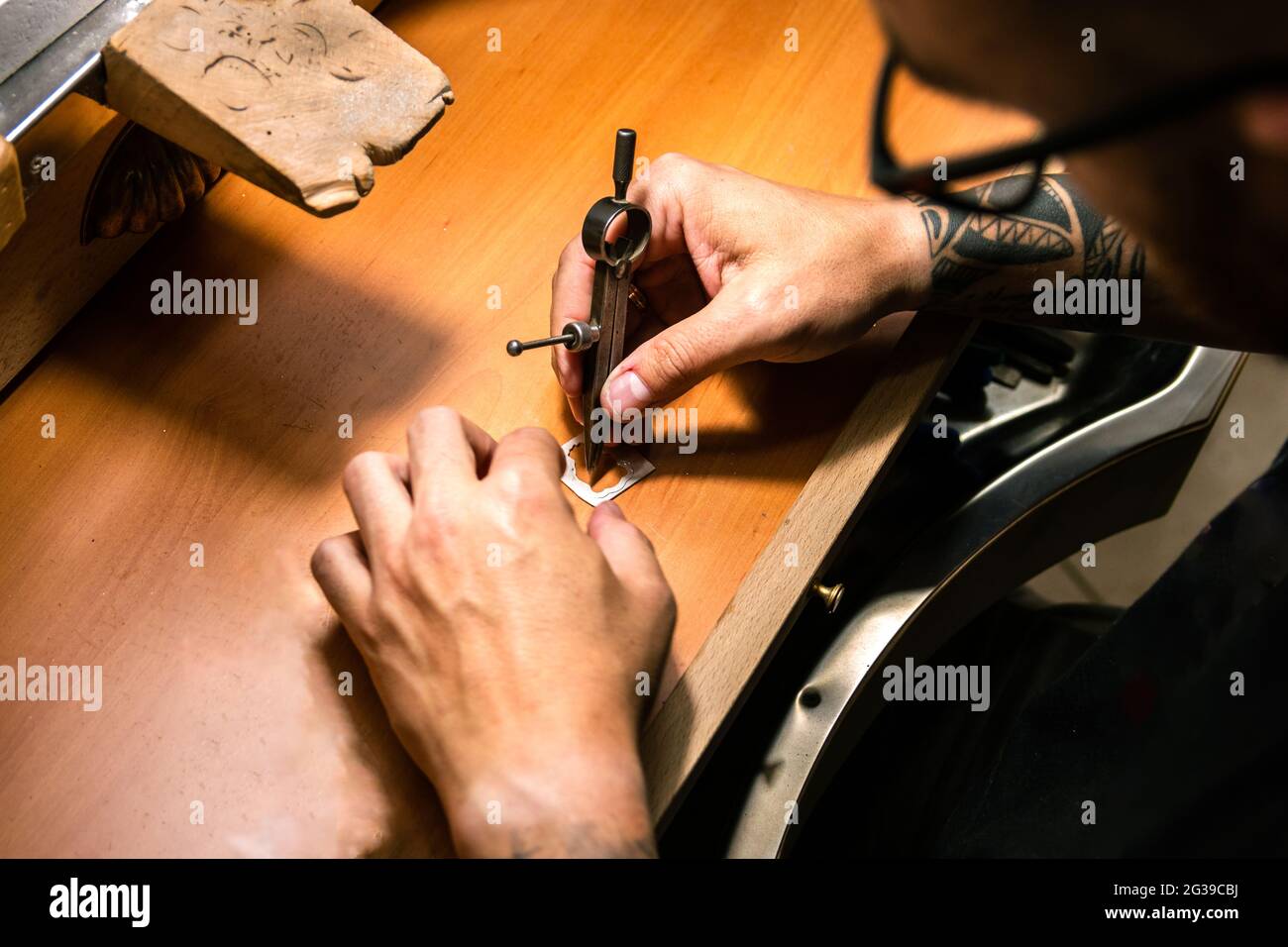 Herrenhände in einer Schmuckwerkstatt, die ein Silberstück mit Kompass markiert Stockfoto