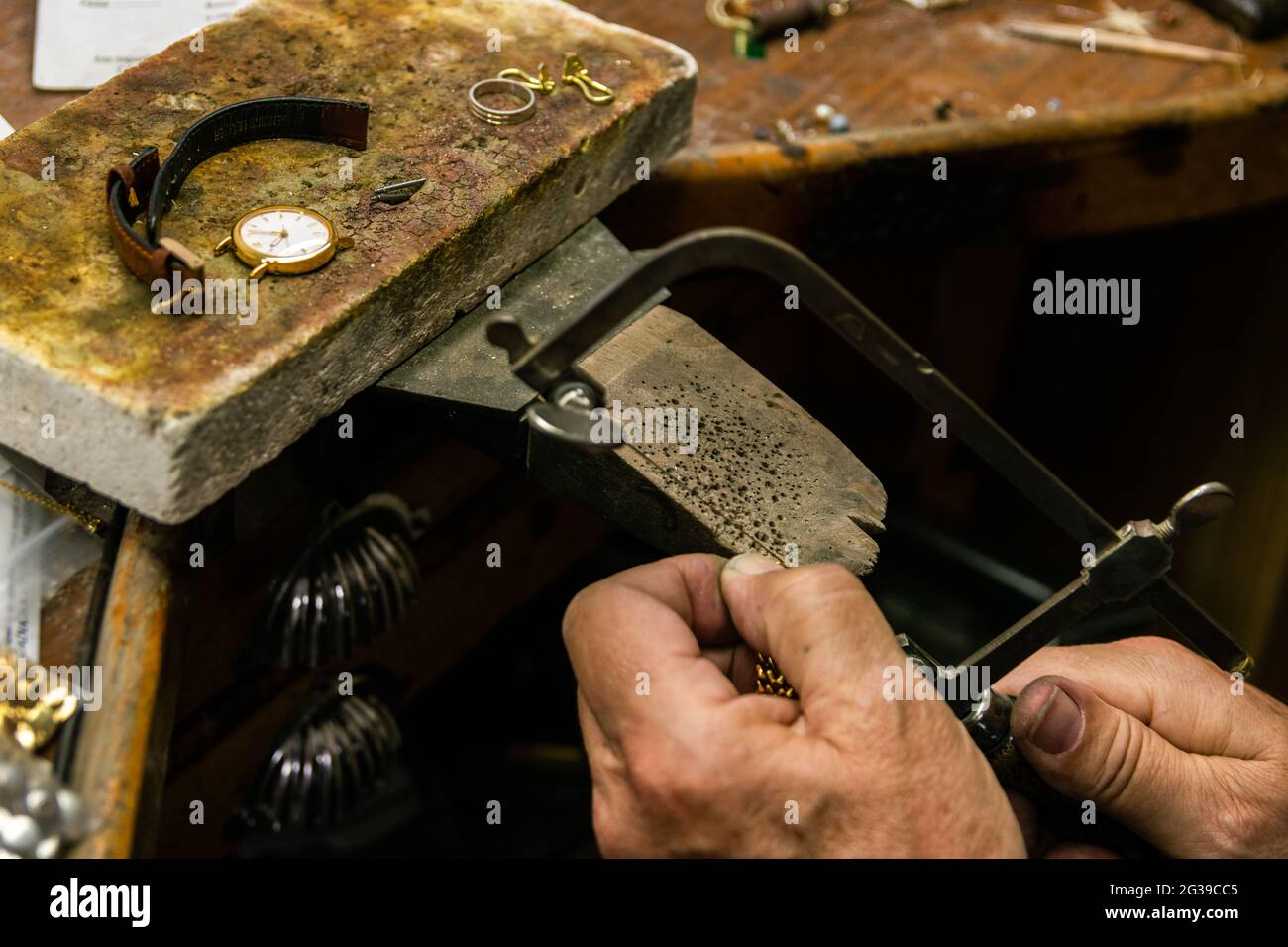 Herrenhände in einer Schmuckwerkstatt schneiden ein Stück Gold mit einer Bügelsäge Stockfoto
