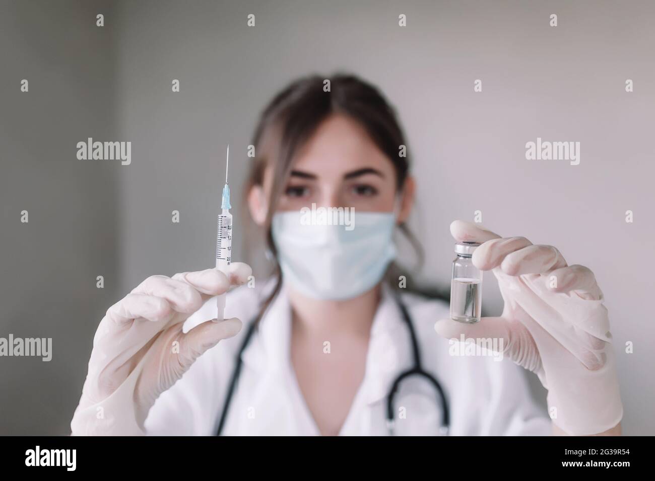Arzt oder Krankenschwester in Schutzmaske und Handschuhen mit Stethoskop hält Glasfläschchen mit Anti-Virus-Impfstoff und Spritze. Hochwertige Fotos Stockfoto