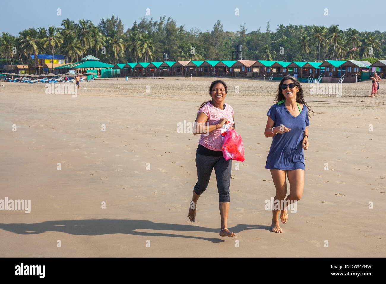 Westernerin und indische Frau joggen fröhlich im Sand am Agonda Beach, Goa, Indien Stockfoto