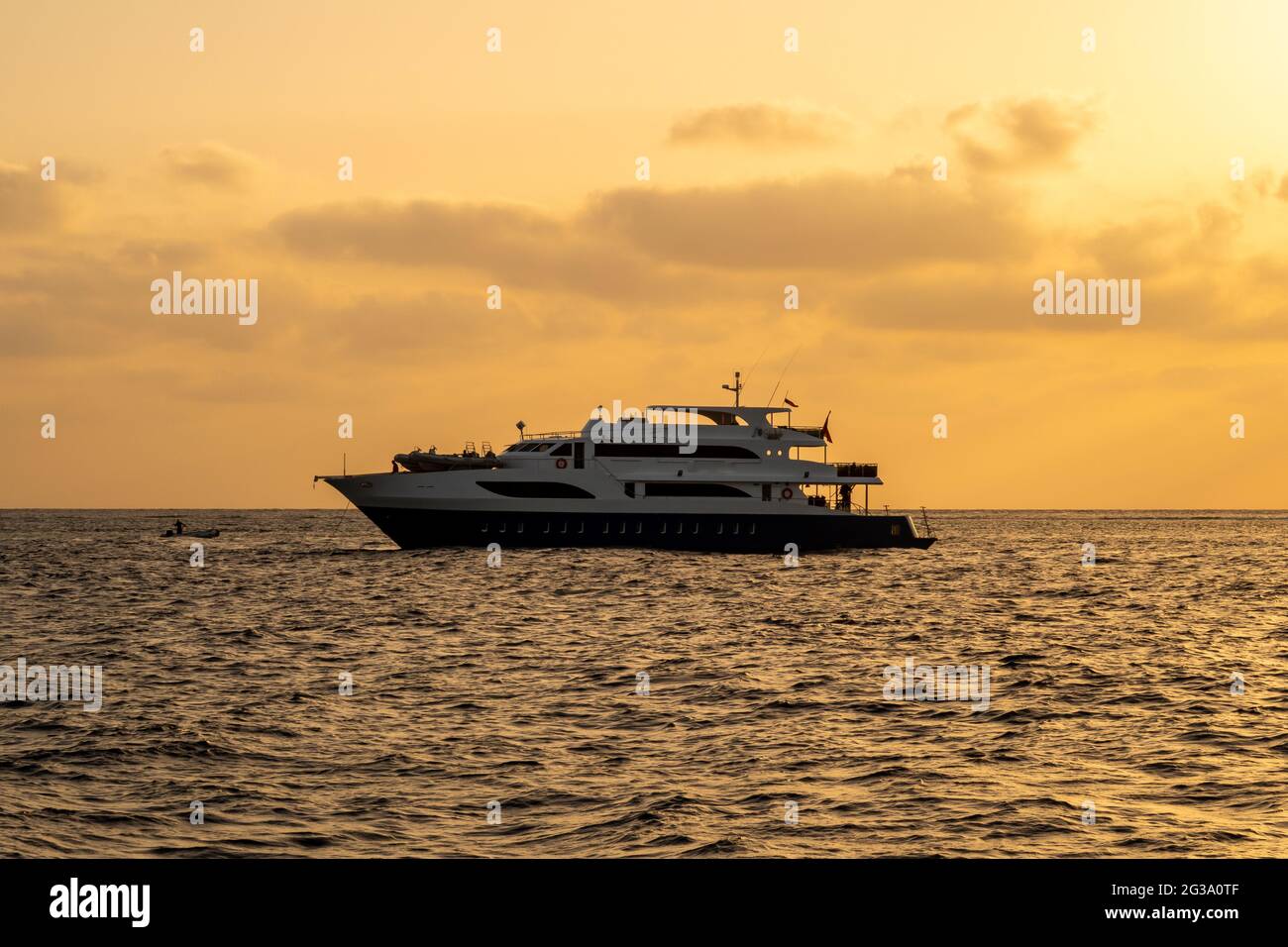 Dunkle Silhouette eines Tauchbootes mit orangefarbenem Sonnenuntergang über dem Roten Meer, bewölktem Himmel und ruhigem Meer. Stockfoto