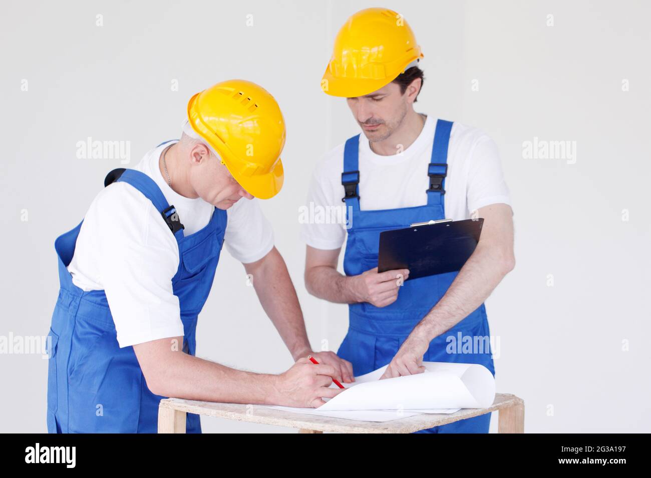 Arbeiter in blauer Uniform und gelben Harthüten mit Blaupause arbeiten auf der Baustelle Stockfoto