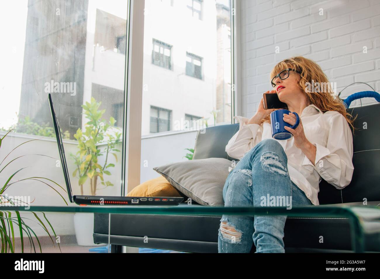 Frau, die zu Hause mit einer Tasse Kaffee und einem Computer telefoniert Stockfoto
