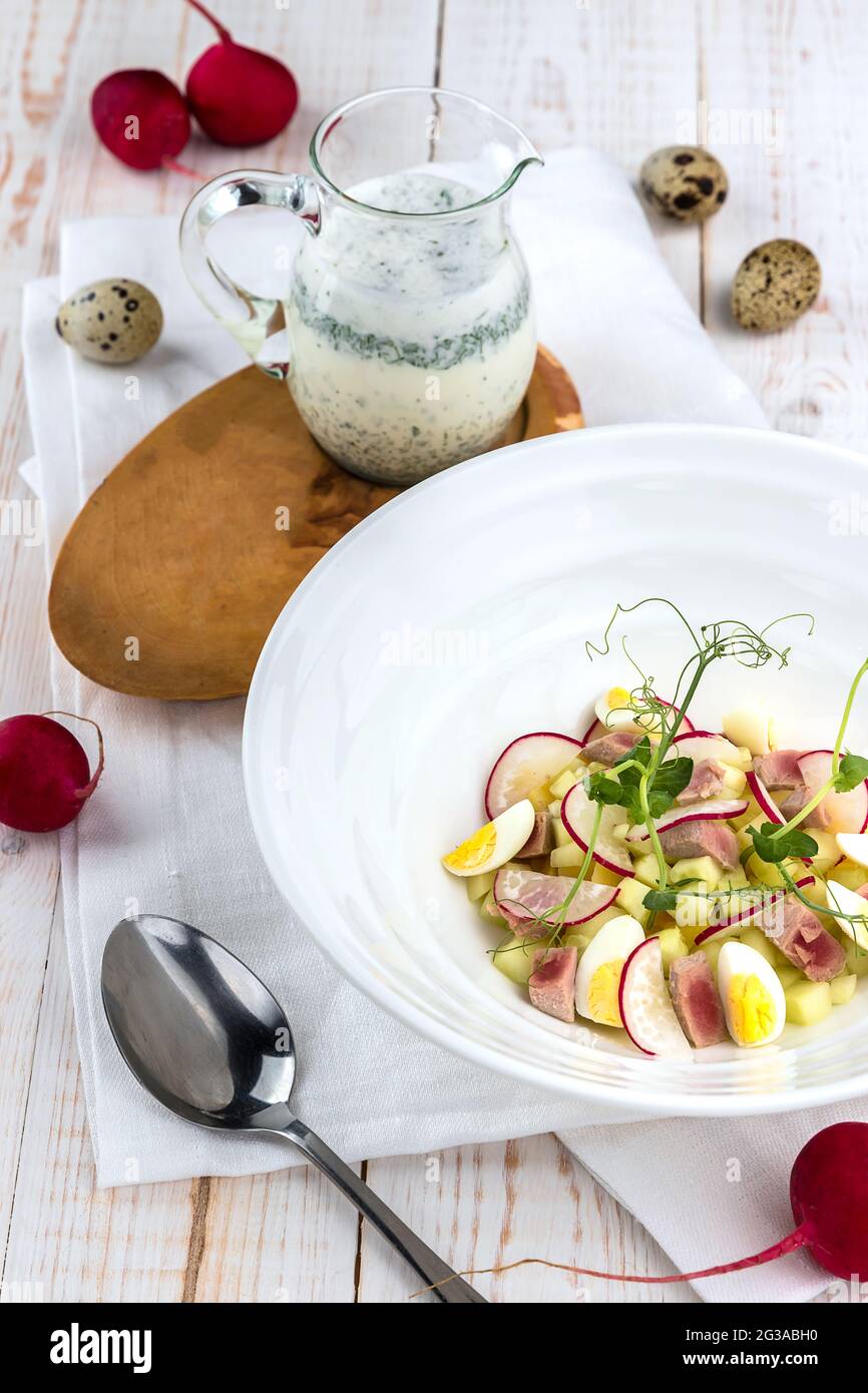 Okroshka auf Kefir mit Thunfisch, Rettich, Wachteleiern auf weißem Holztisch. Kalte Sommersuppe in vielen Ländern Stockfoto