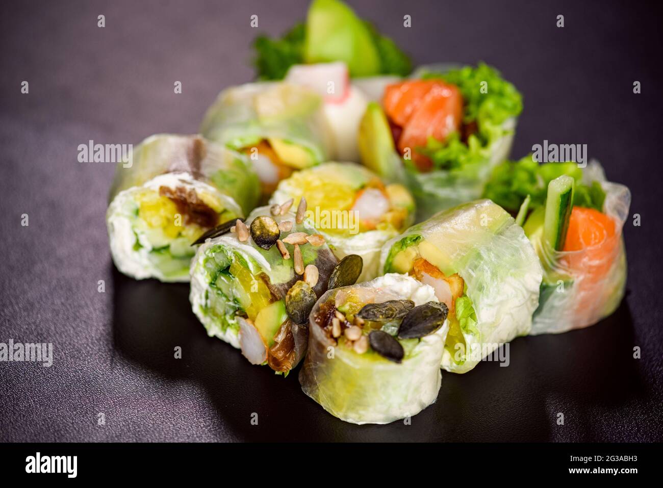 Reispapierrollen mit Lachs, Salat, Garnelen, Gurken, Avocado und Frischkäse philadelphia auf schwarzem Hintergrund. Frühlingsrollen Stockfoto
