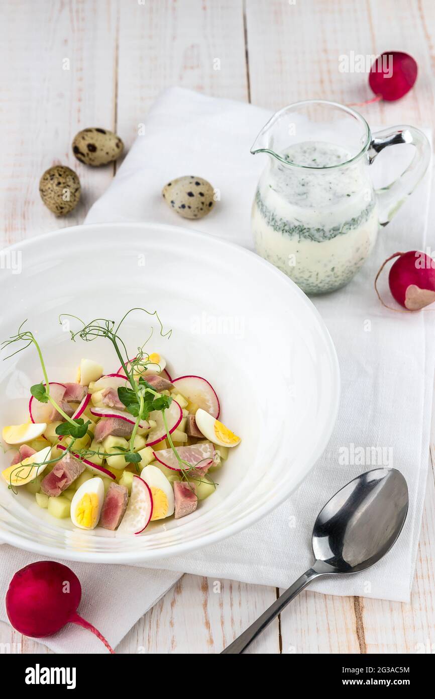 Okroshka auf Kefir mit Thunfisch, Rettich, Wachteleiern auf weißem Holztisch. Kalte Sommersuppe in vielen Ländern Stockfoto