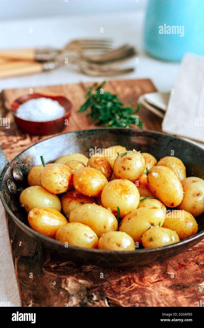 Goldene Babykartoffeln in gusseiserner Pfanne auf Holzbrett mit Kräutern und Salz rösten Stockfoto