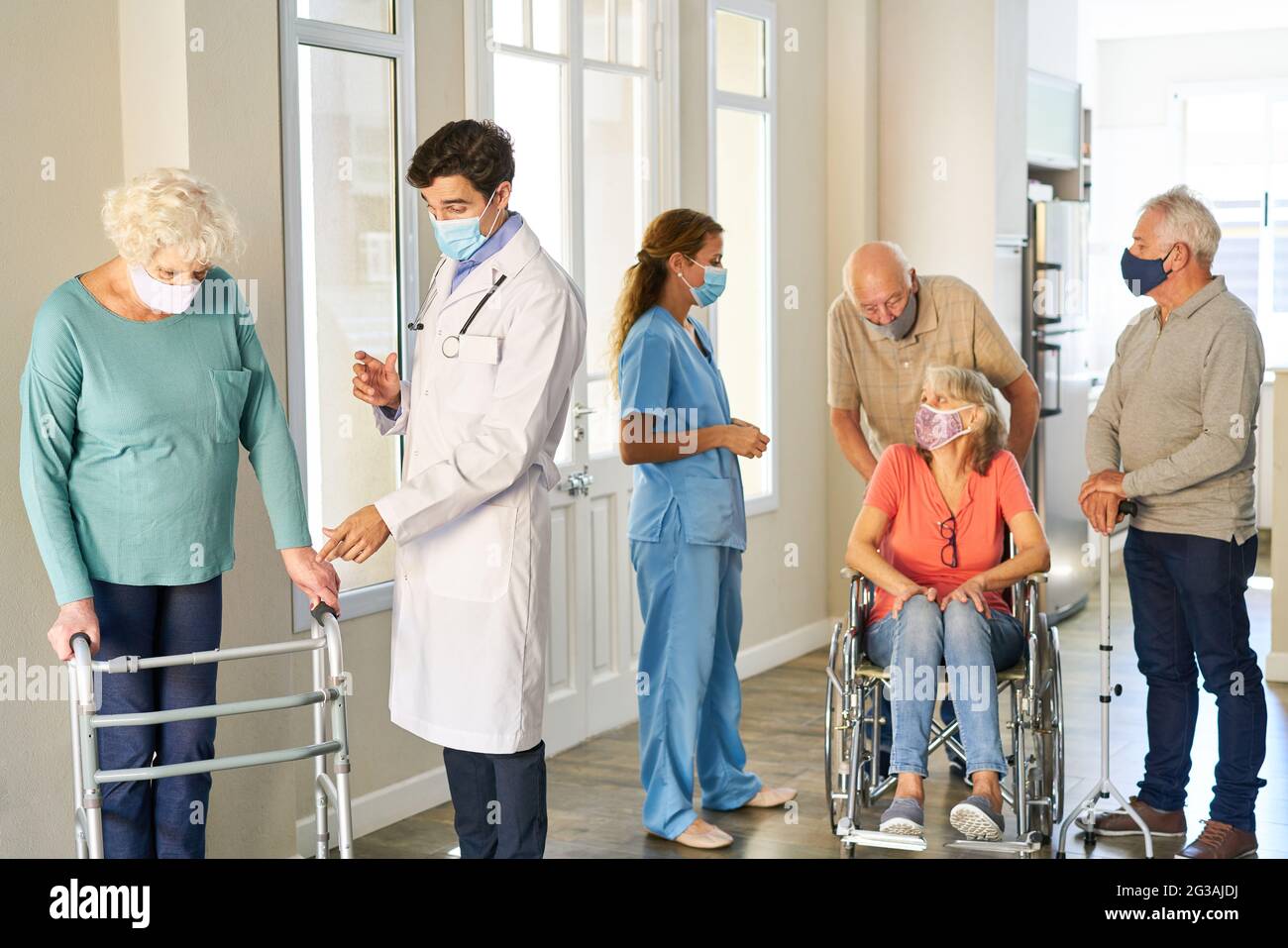 Senioren und Krankenhauspersonal mit Masken wegen Covid-19 im Pflegeheim zusammen mit Smalltalk Stockfoto