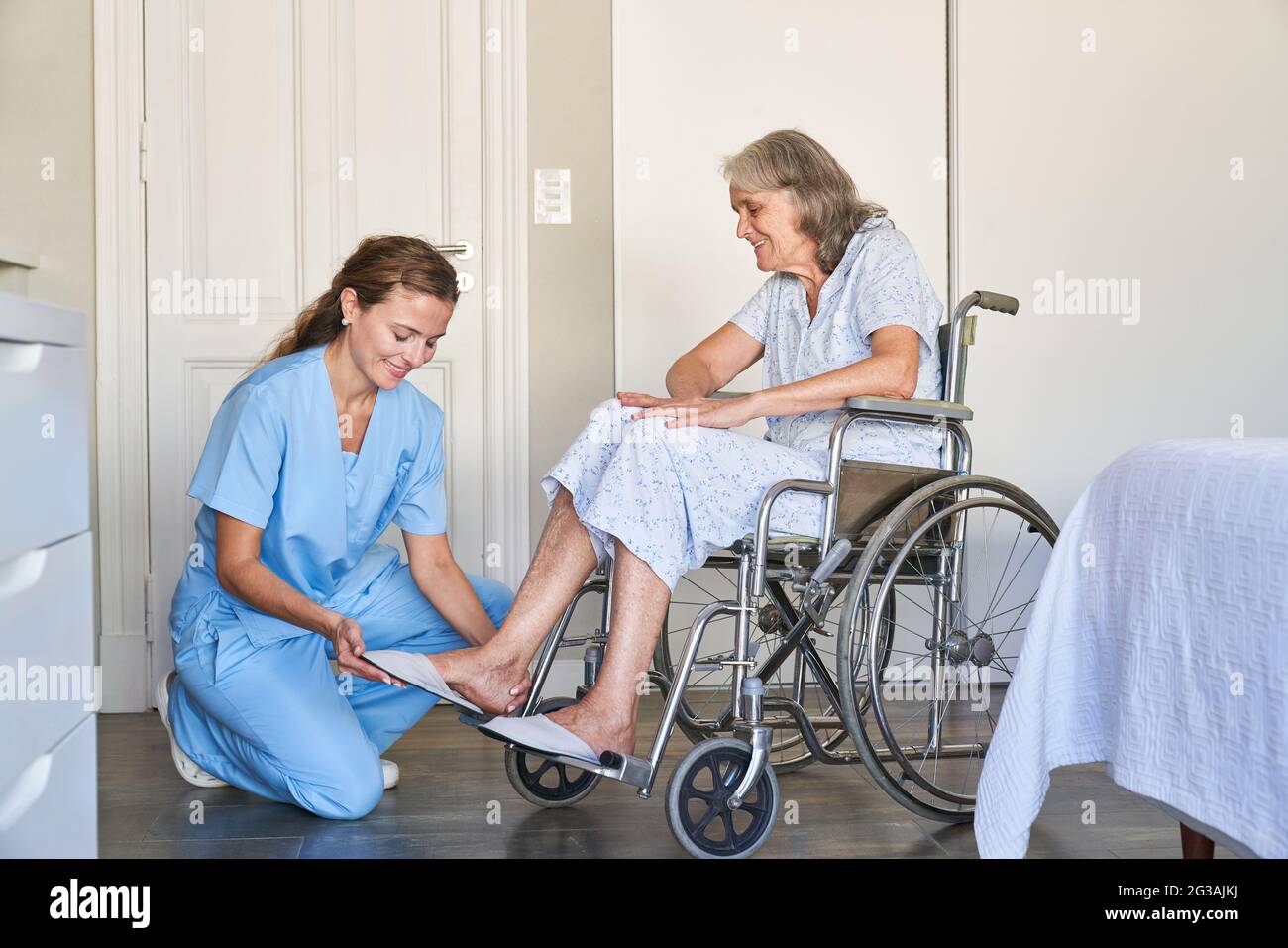 Ältere Pflegekraft hilft älteren Frauen im Rollstuhl, Schuhe an- und auszuziehen Stockfoto