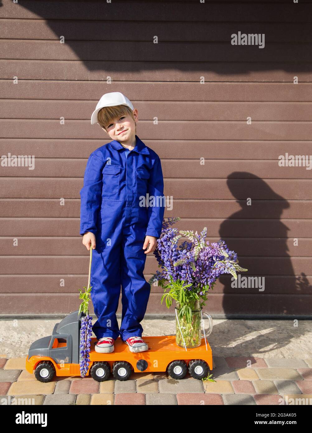Niedlicher Kleinkind Junge In Blauen Overalls Und Mutze Steht Auf Einem Grossen Spielzeug Lkw Mit Einem Blumenstrauss Darauf Lieferkonzept Herzlichen Gluckwunsch Fur Mama Litt Stockfotografie Alamy