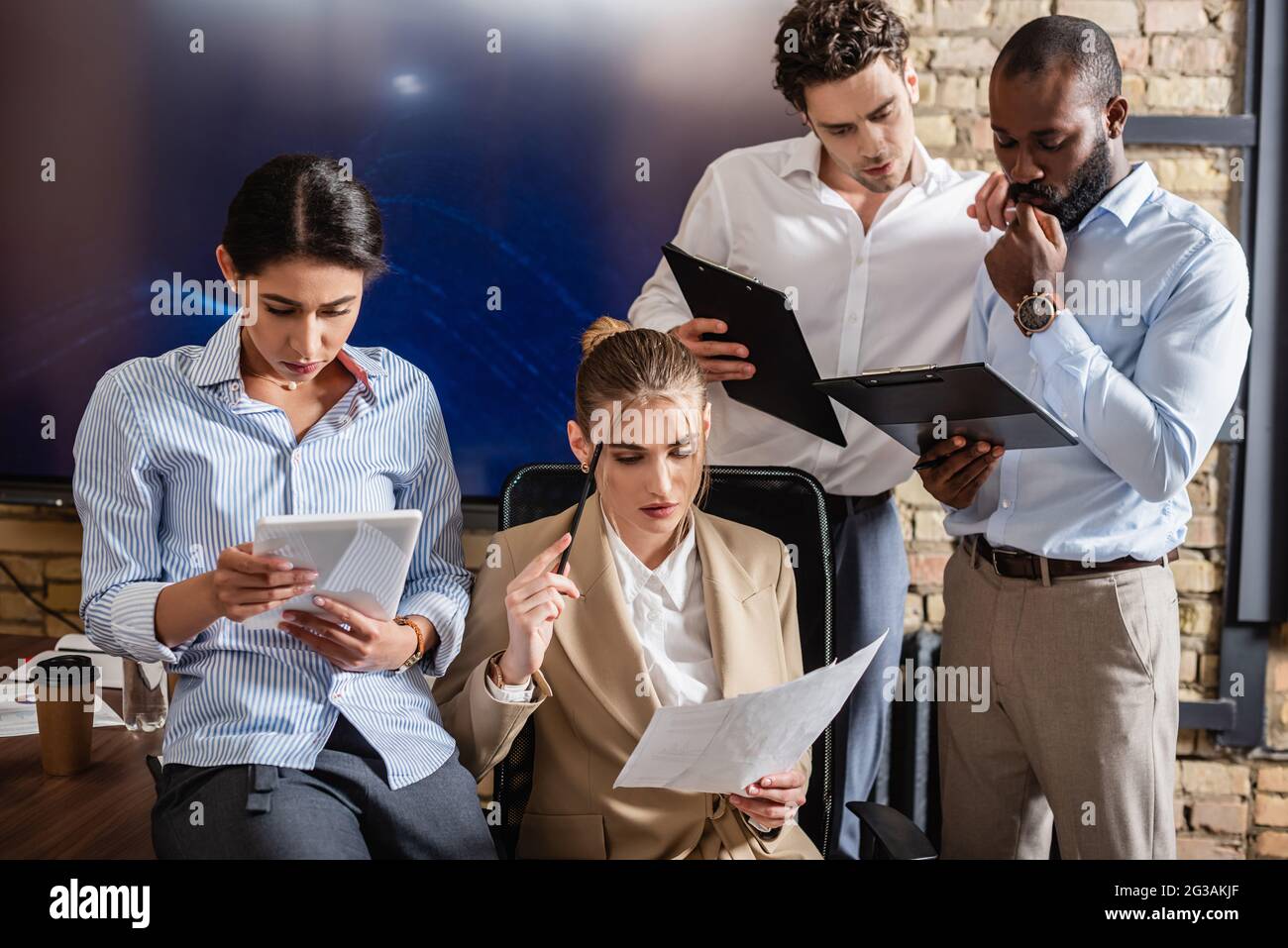 Durchdachte, interrassische Geschäftsleute, die im Konferenzraum mit einem digitalen Tablet und Dokumenten arbeiten Stockfoto