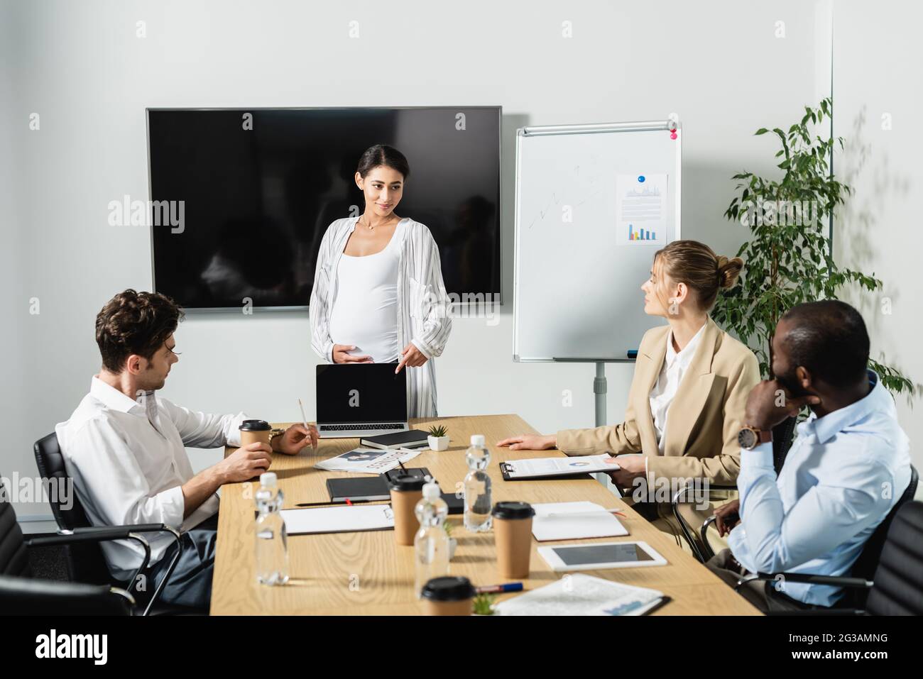 Schwanger afroamerikanische Geschäftsfrau zeigt auf Laptop während der Diskussion mit multiethnischen Kollegen Stockfoto