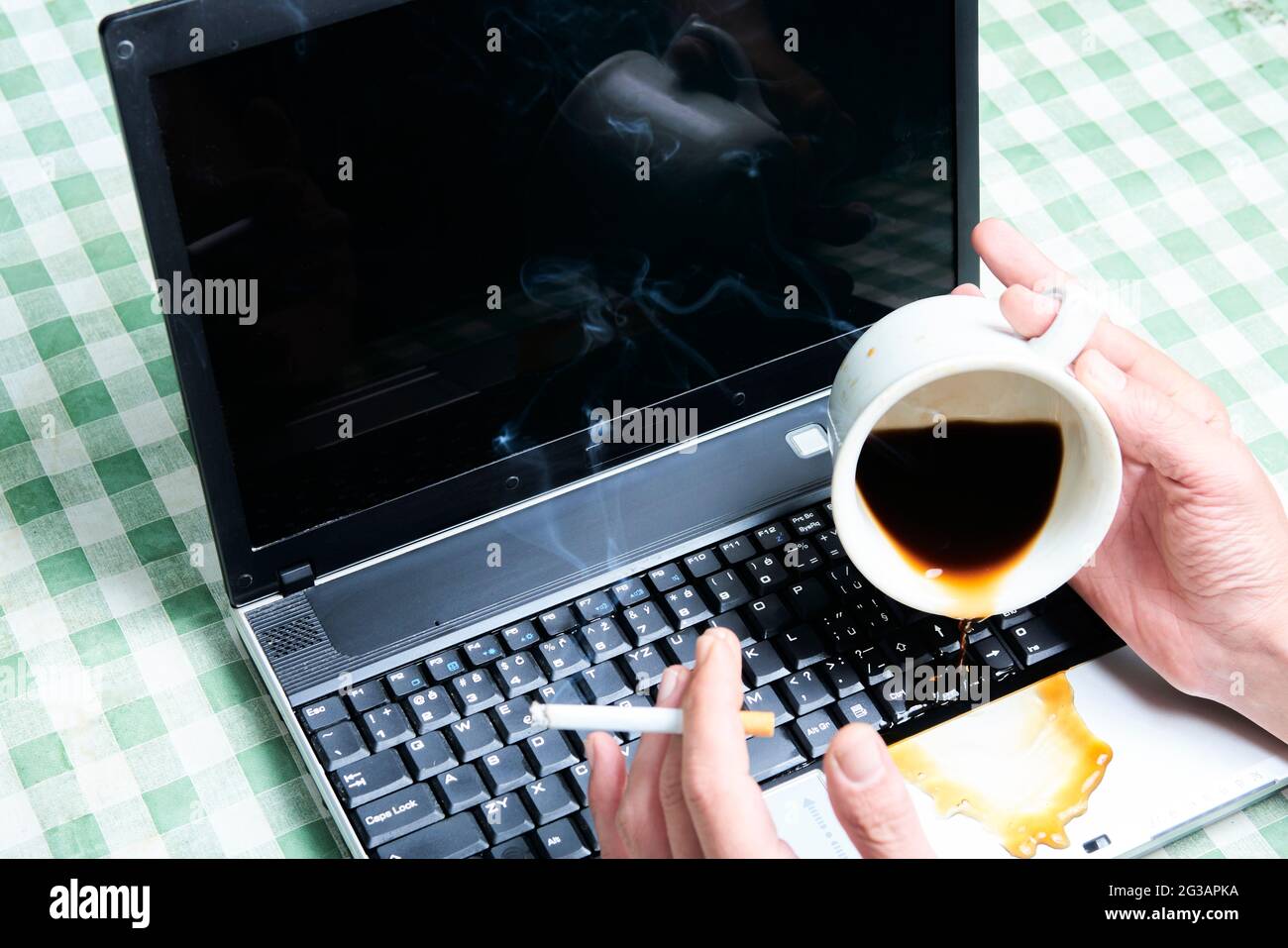 Notizbuch schüttete ungemülich Kaffee aus einer Tasse. Computerunfall. Laptop mit Flüssigkeit zerstört. Kaffee verschüttet auf Laptop-Tastatur. Verschütten von Kaffee Stockfoto