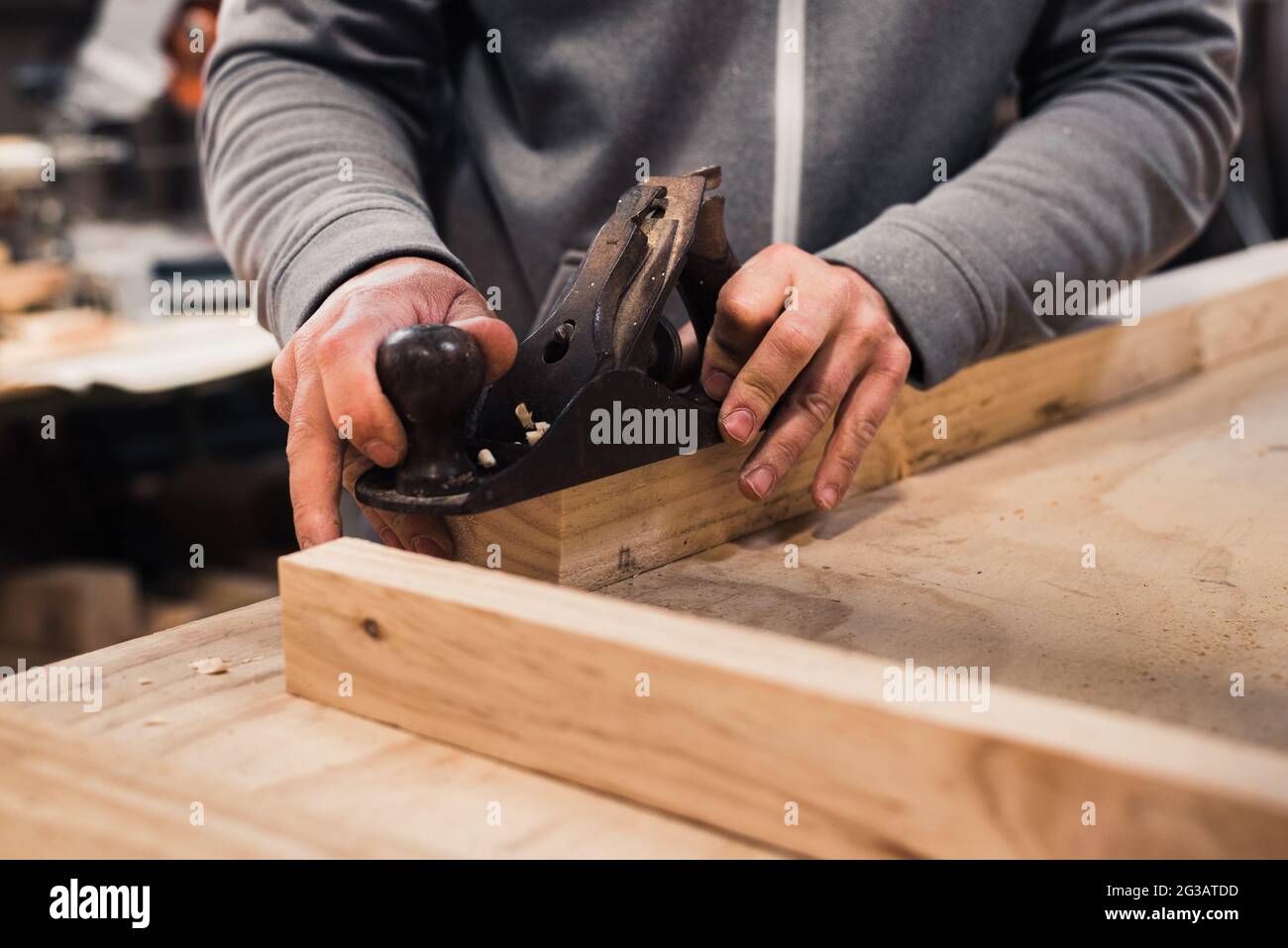 Nahaufnahme der Hände eines Zimmermanns, der mit einem Tischlerpinsel eine Holzlatte hobelt Stockfoto