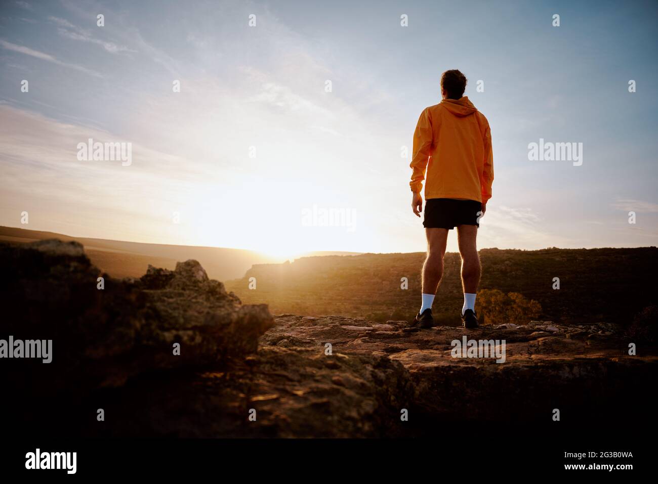 Rückansicht eines jungen männlichen Athleten, der den wunderschönen Sonnenaufgang nach dem morgendlichen Lauf während des Bergpfades beobachtet Stockfoto