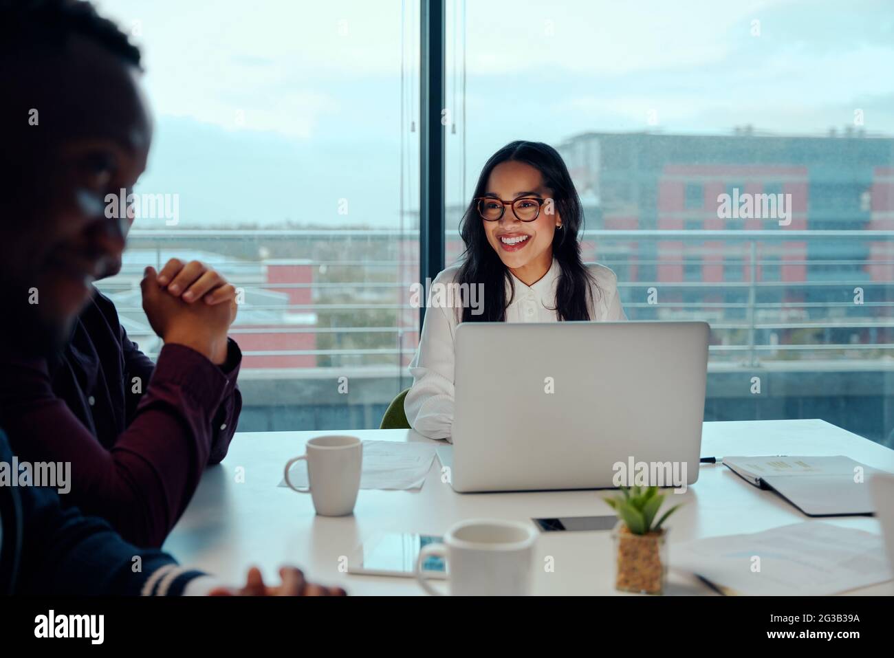 Erfolgreiche lächelnde junge Frau, die bei einem Geschäftstreffen mit seinen multiethnischen Kollegen sitzt Stockfoto