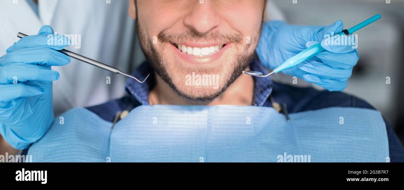 Nicht erkennbarer männlicher Patient mit Zahnaufhellung Verfahren in der modernen Zahnklinik, lächelnd an der Kamera, Zahnarzt Hände in Gummihandschuhe mit Zahn zu Stockfoto