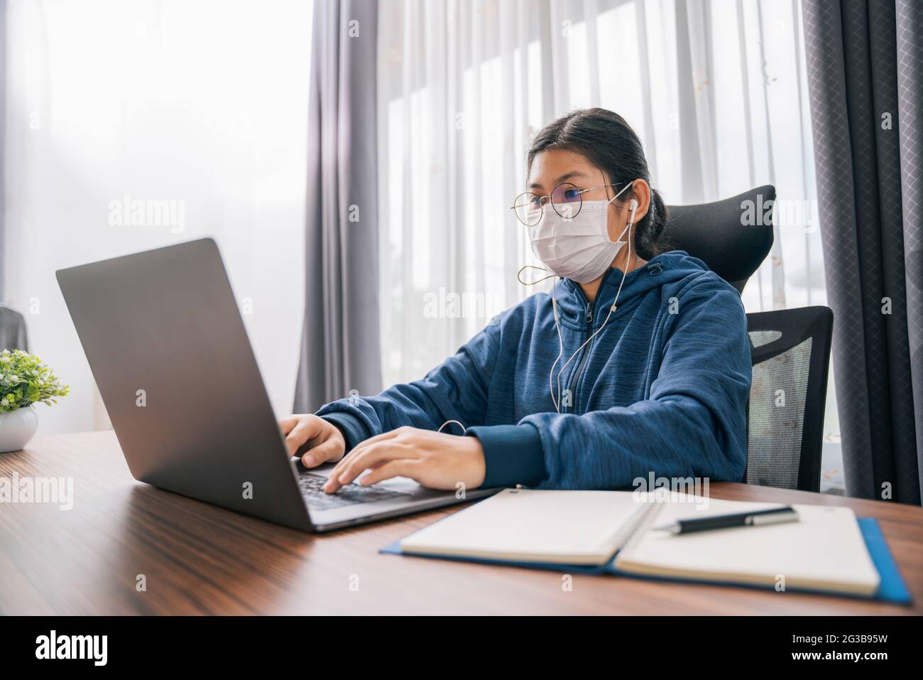 Asiatische Teenager-Mädchen tragen Kopfhörer Sprache online lernen, mit Laptop, Blick auf den Bildschirm, tun Schulaufgaben zu Hause, Notizen schreiben, zuhören Stockfoto