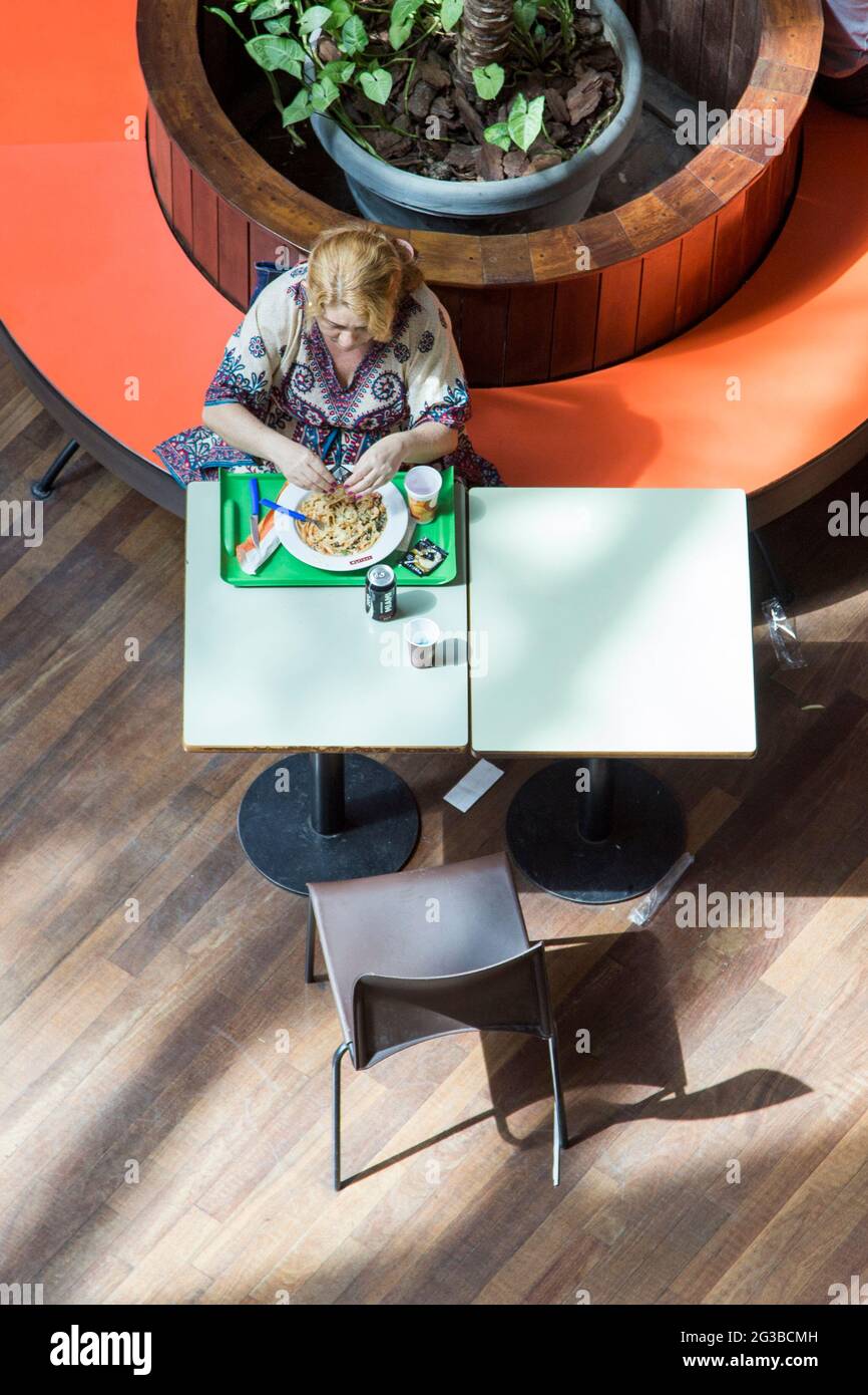 Eine Frau, die in einem Lebensmittelbereich eines Einkaufszentrums zu Mittag gegessen hat Stockfoto
