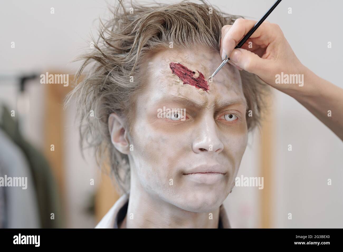 Junger Mann mit Zombie Make-up, der vor dem Schießen eine Wunde auf seine Stirn gemalt hat Stockfoto