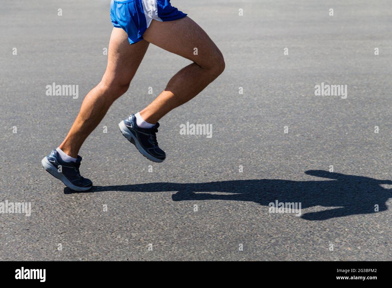 Beine männlicher Läufer-Athlet läuft auf grauem Asphalt Stockfoto