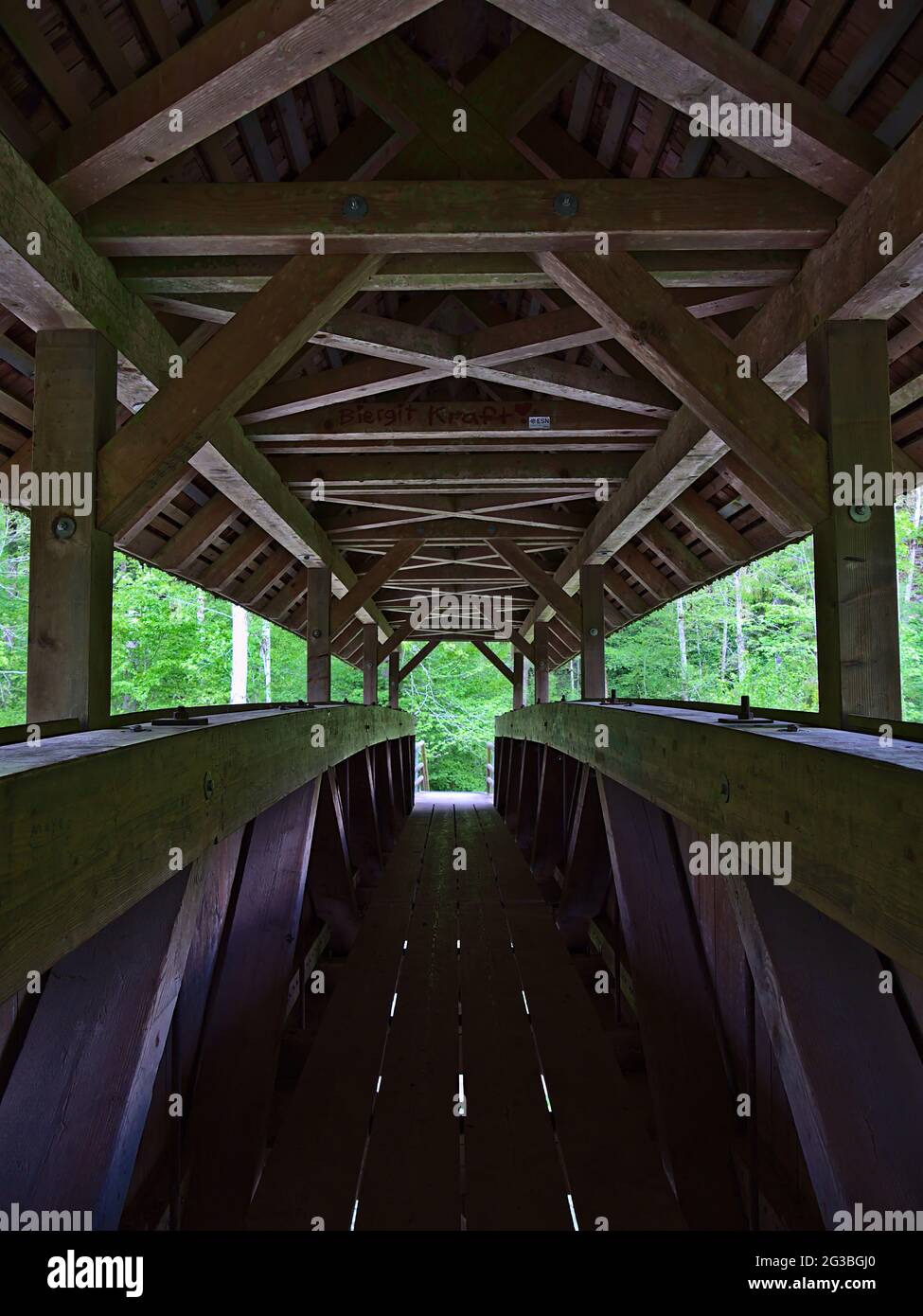 Symmetrische Ansicht mit abnehmender Perspektive auf das Innere einer überdachten Holzbrücke, die den Fluss in der Wutachschlucht überquert. Stockfoto