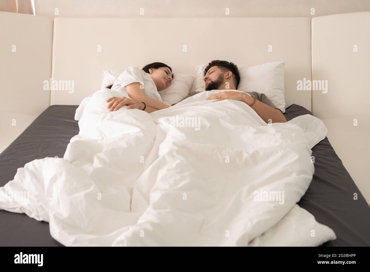 Modernes junges, gerade verheiratetes Paar, das unter einer weißen Decke schläft Stockfoto