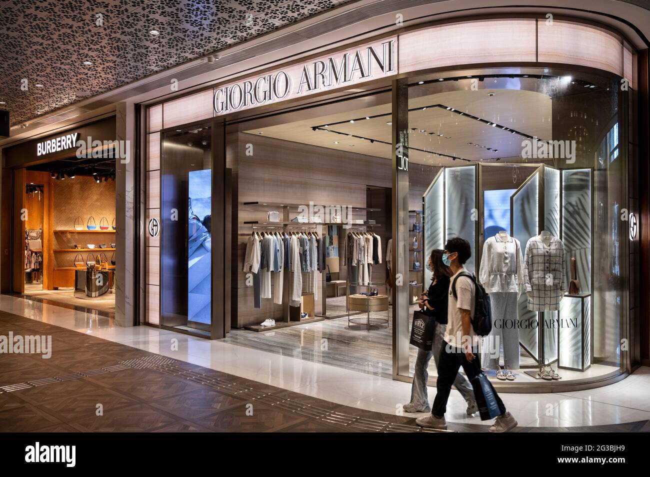Ein Paar, das in einem Einkaufszentrum an den Geschäften der italienischen Luxusmodemarke Giorgio Armani und der britischen Luxusmodemarke Burberry in Hongkong vorbeiging. Stockfoto