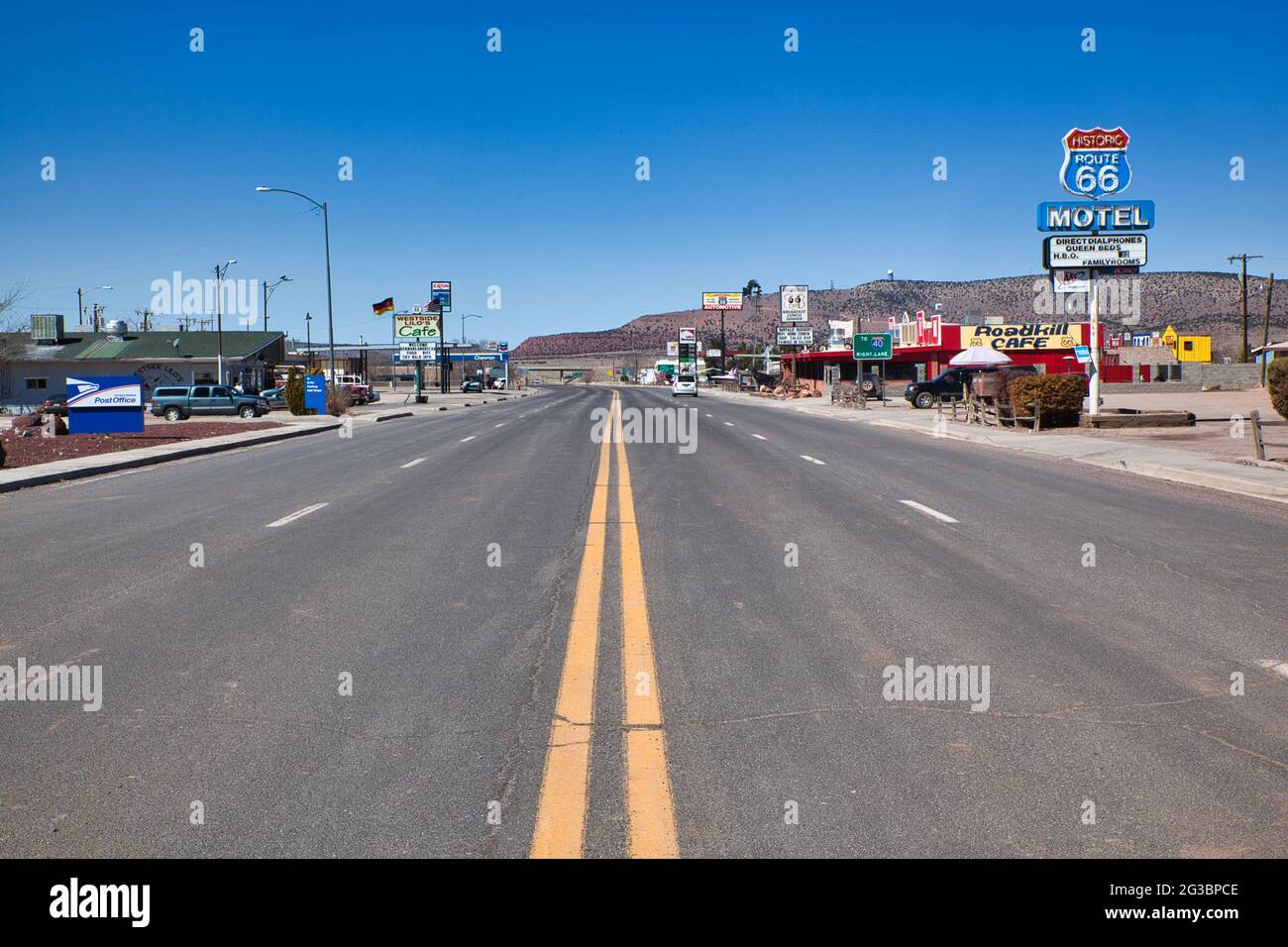 Blick geradeaus auf die zentralen gelben Linien eines Abschnitts der Route 66, wo sie durch eine kleine Stadt mit Motel- und anderen Schildern nach Arizona, USA, führt Stockfoto