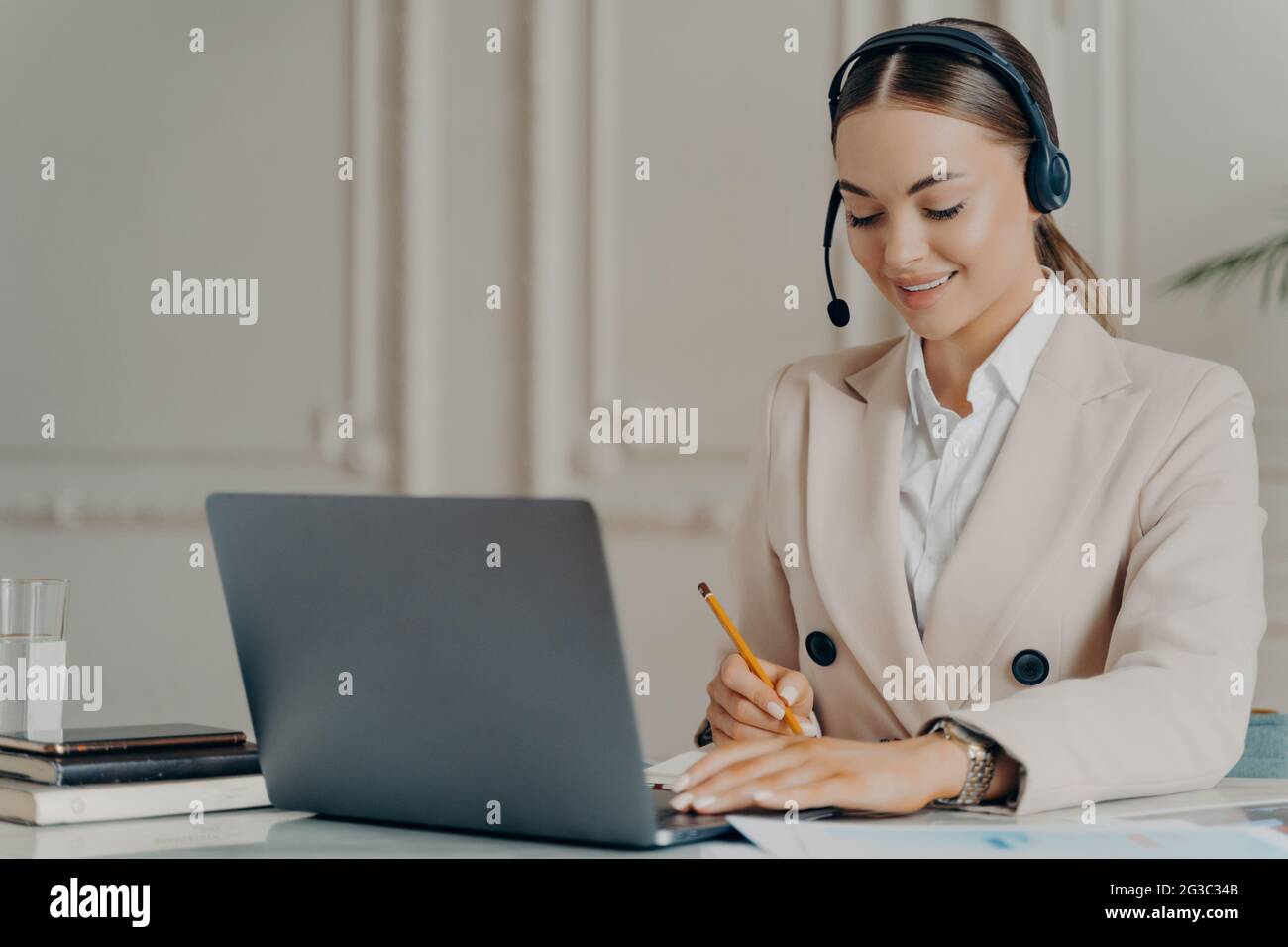 Positive junge Geschäftsfrau mit Headset, die an einer Webkonferenz teilnimmt Stockfoto