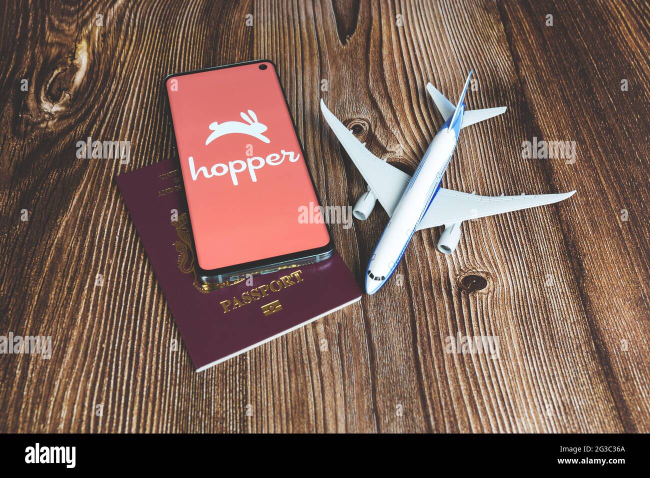 Smartphone mit Hopper App Logo mit Flugzeugspielzeug und rotem Pass auf Holzhintergrund. Reise-Anwendung, Urlaubsplanung Stockfoto