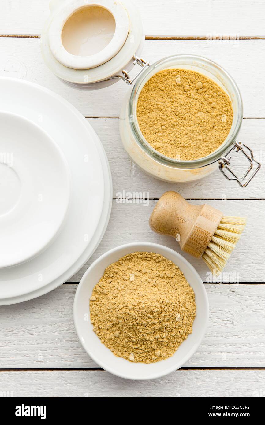 Waschen der Gerichte mit Senfpulver Konzept. Weiße saubere Teller mit Schale und Glas aus gelbem Senfpulver und Holzwaschbürste und Klasse Stockfoto